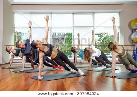 A Group Of Sporting Young People In Sportswear, In A Fitness Room, Doing Push-ups Or Planks In The G