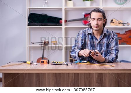 Young handsome repairman repairing violin