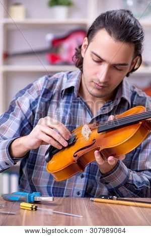 Young handsome repairman repairing violin