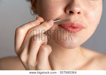 A Young Woman Plucks Her Hair Over Her Upper Lip With Tweezers. The Concept Of Getting Rid Of Unwant