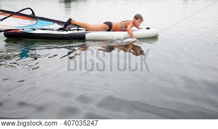 Active Senior Woman In Swim Suit Ride Lying On Windsurfing In The Water