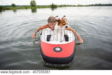 Active Senior Woman In Swim Suit Lying On Surf With Dog In The Water