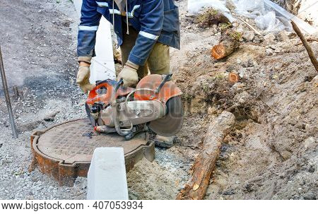 A Worker Repairs A Section Of A Road, Cuts Out Worn Asphalt With A Portable Concrete Cutter And Diam