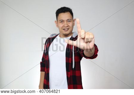 Portrait Of Asian Man Looking To Camera And Posing With L Shape Fingres, Smiling Expression