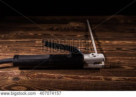 Welding Electrode Holder With Electrode On A Wooden Background. Studio Photo In Hard Light.