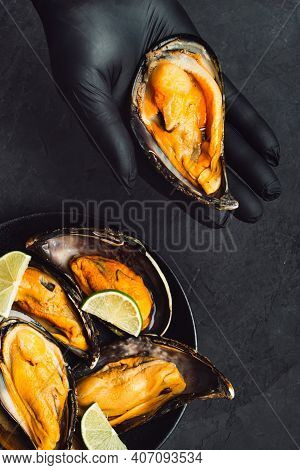 Large Mussels In A Hand In A Black Glove. Close Up. Top View.