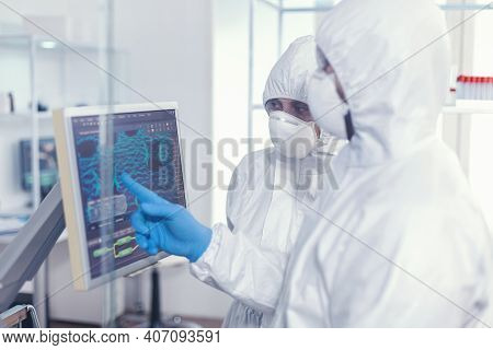 Chemist In Ppe Suit Explainig To Doctor Vaccine Development In Modern Equipped Laboratory Pointing O
