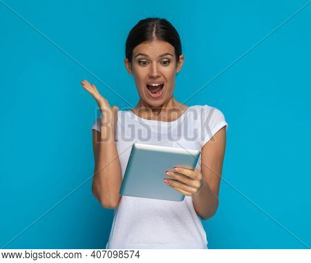 beautiful casual woman is happily surprised about something on his tablet against blue background