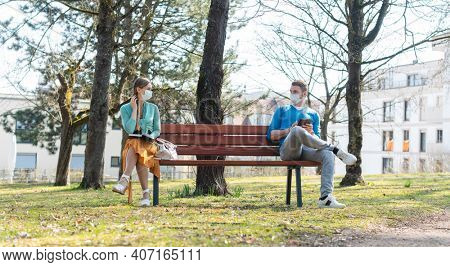 Woman and man with face mask in social distancing flirting sitting on a park bench