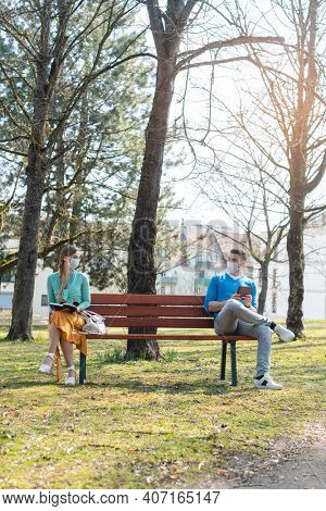 Woman and man with face mask in social distancing flirting sitting on a park bench