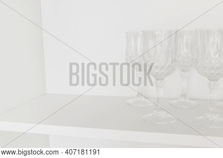 Dishes In The Kitchen. Transparent Glass Wineglass, Stand On A White Shelf In A Kitchen Cabinet. Sel