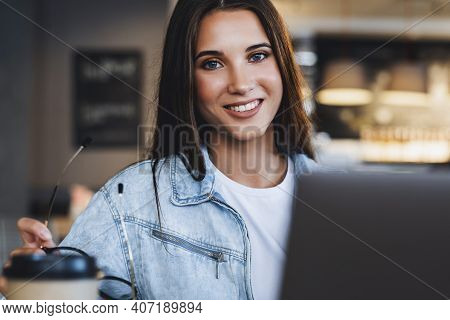 Femalesmiling And Looking At The Camera. Attractive Business Woman Sits At Table In Front Of Laptop 