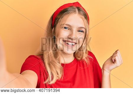 Beautiful young caucasian girl taking a selfie photo screaming proud, celebrating victory and success very excited with raised arm 