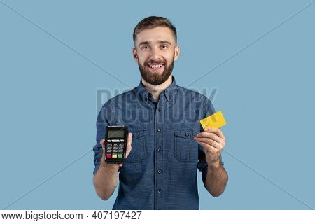 Portrait Of Happy Young Guy Holding Credit Card And Payment Terminal, Amiling And Looking At Camera 