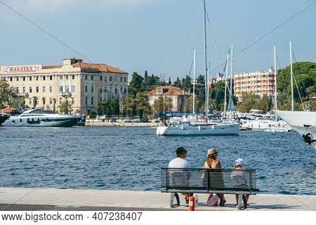 Zadar, Croatia - Aug 13, 2020: Family Rest On Bench By Old Town Harbour In Afternoon