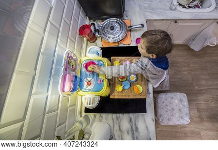 Child Boy Playing With Toy Kitchen Over Real Kitchen Countertop. Overhead Wide Angle Shot. Slighly M