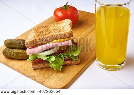 Sandwich With Ham, Vegetables On A Chopping Board And A Glass Of Orange Juice.