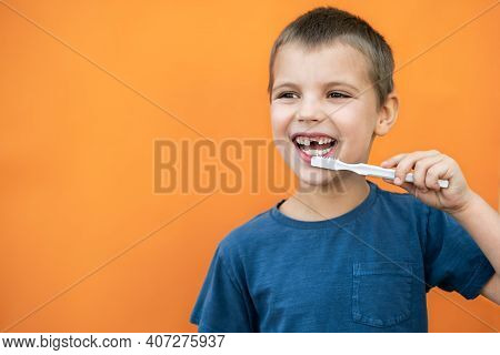 Boy Without Milk Upper Tooth In Blue T-shirt Holds Toothbrush In Hand On The Orange Background. Copy