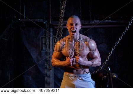Primal Instinct. Angry Muscular Man Screaming At Camera And Breaking Chains On Chest, Dark Backgroun
