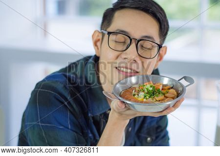 Young Man Wearing Glasses Holding The Fried Egg Served On A Pan With Colorful Toppings Served On A P