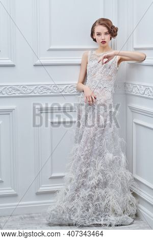 Beautiful girl in a luxury white evening dress in a classic white interior. Fashion shot. Hair and makeup in the style of the 20s. 