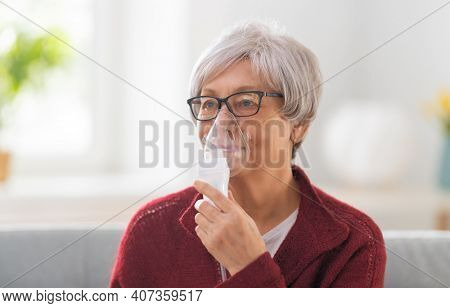 Elderly woman using inhaler for asthma and respiratory diseases at home.