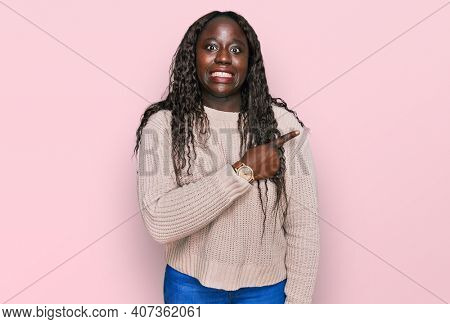 Young african woman wearing wool winter sweater pointing aside worried and nervous with forefinger, concerned and surprised expression 