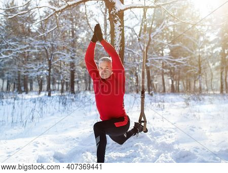 Outdoor Winter Fitness Concept. Sporty Senior Man Training With Resistance Straps At Snowy Forest. F