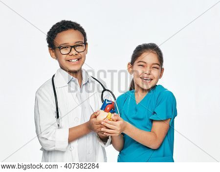 Two Positive Kids Wearing A Medical Uniform Are Holding An Anatomical Model Of Heart. Cardiac Care C