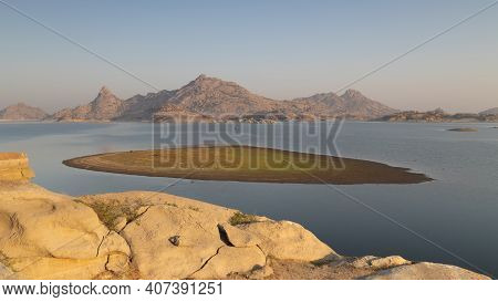 Landscape Of Jawai Dam With Water, Clear Blue Sky And Aravalli Mountain Ranges With Its Reflection I