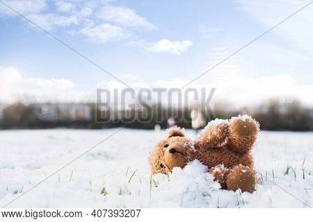 Lost Teddy Bear With Sad Face Lying On Snow With Blurry People,lonely Bear Doll Laying Down On The P
