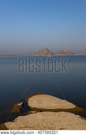 Landscape Of Jawai Dam With Water, Clear Blue Sky And Aravalli Mountain Ranges With Its Reflection I