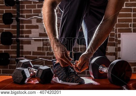 Fitness Motivation And Muscle Training Concept. Man In Sneakers Tying Shoelaces In Sunlight. Athlete