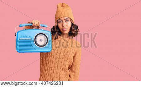 Young beautiful mixed race woman holding vintage radio thinking attitude and sober expression looking self confident 