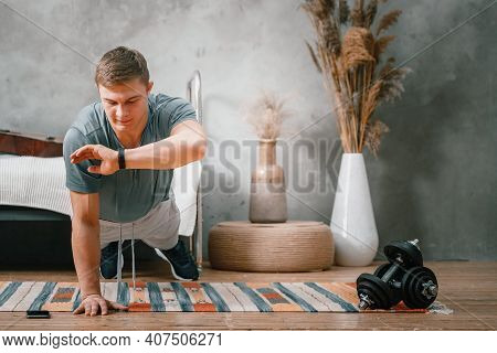 Young Man Goes In For Sports At Home, Training Online. The Athlete Makes A Plank, Looks At The Time 