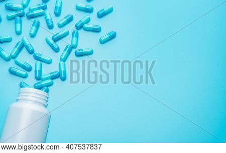 Blue Capsules Pill Spilled Out From White Plastic Bottle Container On Blue Background With Space For