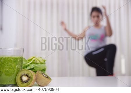 Green Smoothie With Focused Kiwis And Woman Exercising On Unfocused Background