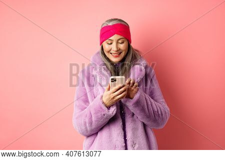 Online Shopping And Fashion Concept. Modern Asian Granny In Trendy Faux Fur Coat Texting Message, Us