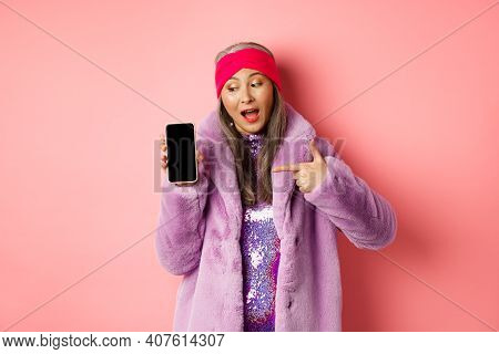 Online Shopping And Fashion Concept. Cool Asian Granny In Stylish Faux Fur Coat Pointing Finger Left