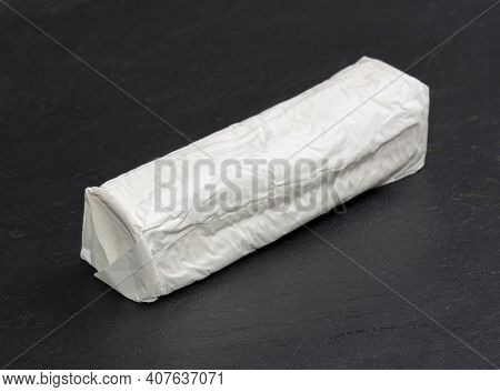 Goat Cheese Roller Wrapped In Paper. Isolated Over Black Slate