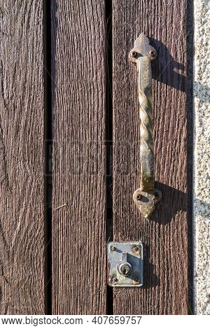Old Plank Door With An Ancient Rusty Iron Ornamental Handle And A Peeling Keyhole. Rusty Screws. Vin