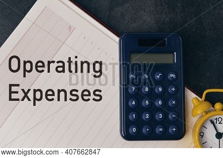 Top View Of Clock, Calculator And Notebook Written With Text Operating Expenses