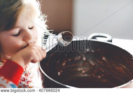 Cute Toddler Girl Eating Chocolate Dough Rests With Spoon And Fingers From Pot. Happy Child Licking 