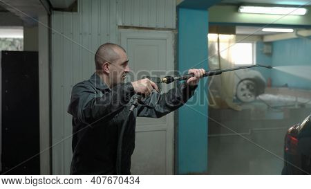 A Caucasian Man Works In A Car Wash Service. A Man In A Worker's Uniform Holds A Water Gun And Washe