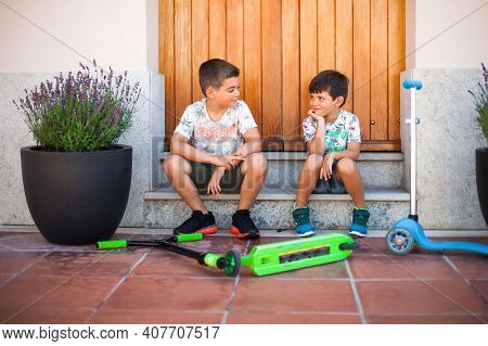Two Smiling Caucasian Children, Sitting On Some Stairs In Front Of A House, Outdoors, With Their Sco