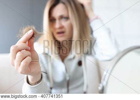 Frustrated Woman Holds Bun Of Her Hair In Her Hand. Hair Loss Concept