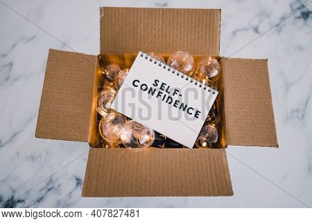 Positive Attitude Concept, Self--confidence Text On Notepad Surrounded By Light Bulbs In Open Box Sy