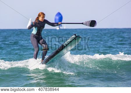 Young Girl With Wetsuit On Inflatable Surfboard Paddle Surf Falling Into The Water. Loss Of Balance 