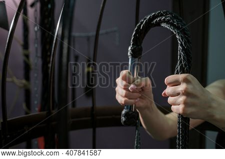 Female Hand With A Long Woven Leather Lash In A Cage. Bdsm Punishment And Pleasure. Cropped.