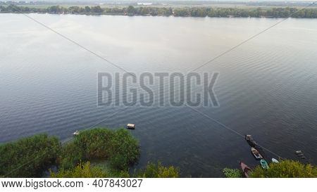 Drone Fly Over Waving River Of Blue Color Surrounded By Local Village With Various Buildings And Wet